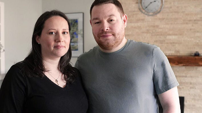 Couple standing together indoors, looking at the camera.